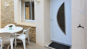 Un bâtiment en pierre avec une porte blanche, une fenêtre et un petit espace extérieur aménagé avec une table et des chaises.