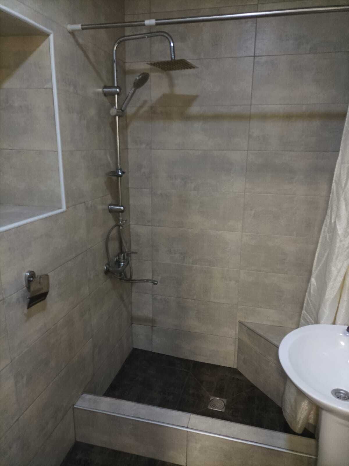 A small, tiled shower area with a handheld showerhead and a wall-mounted faucet.