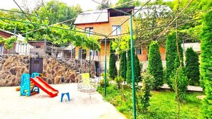 A courtyard with a playground, a stone wall, and a building with a sloped roof. - Cozy Corner (Borjomi)