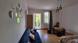 A spacious room with a blue sofa, a wooden table, and a view of greenery outside. - Cozy Corner (Borjomi)