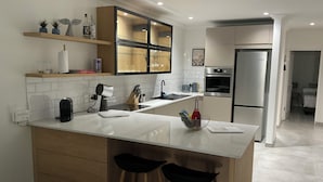 Eine moderne Küche mit einer zentralen Kochinsel, Holzbarhocker, einem Einbauofen und einem Kühlschrank.