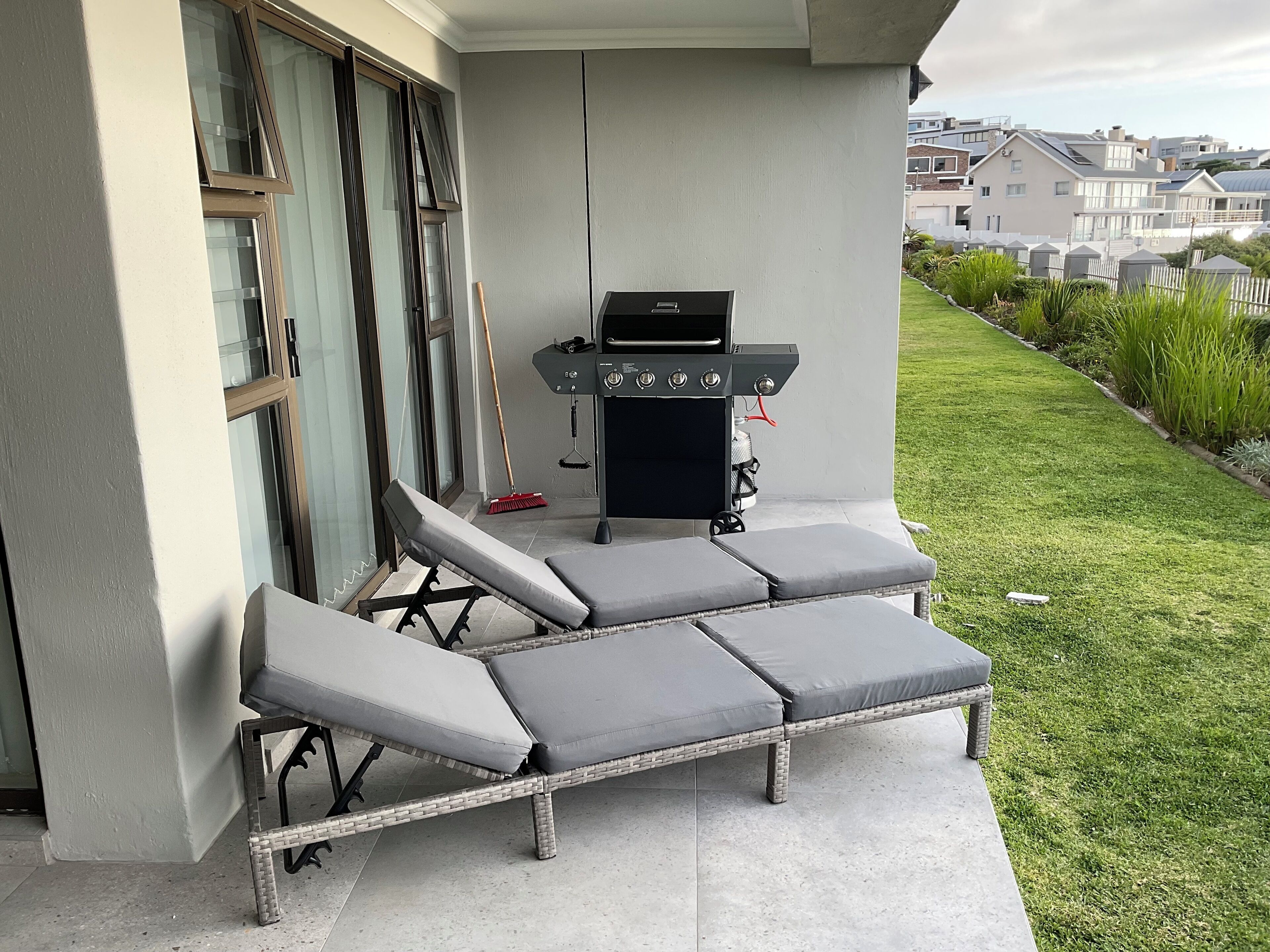 A patio with a grill, lounge chairs, and a broom.