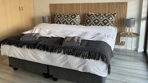 Ein modernes Schlafzimmer mit einem großen Bett, zwei Nachttischlampen, einem Holzschrank und einem gemusterten Kopfteil.