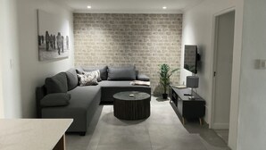 Ein modernes Wohnzimmer mit einem grauen Ecksofa, einem runden Couchtisch und einem flachbildfernseher, der an der Wand montiert ist.