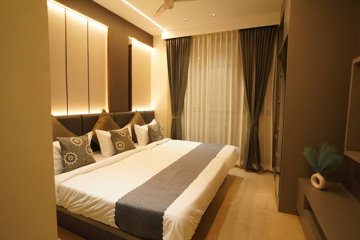 A modern hotel room with a large bed, built-in headboard, and a bedside table with a vase.