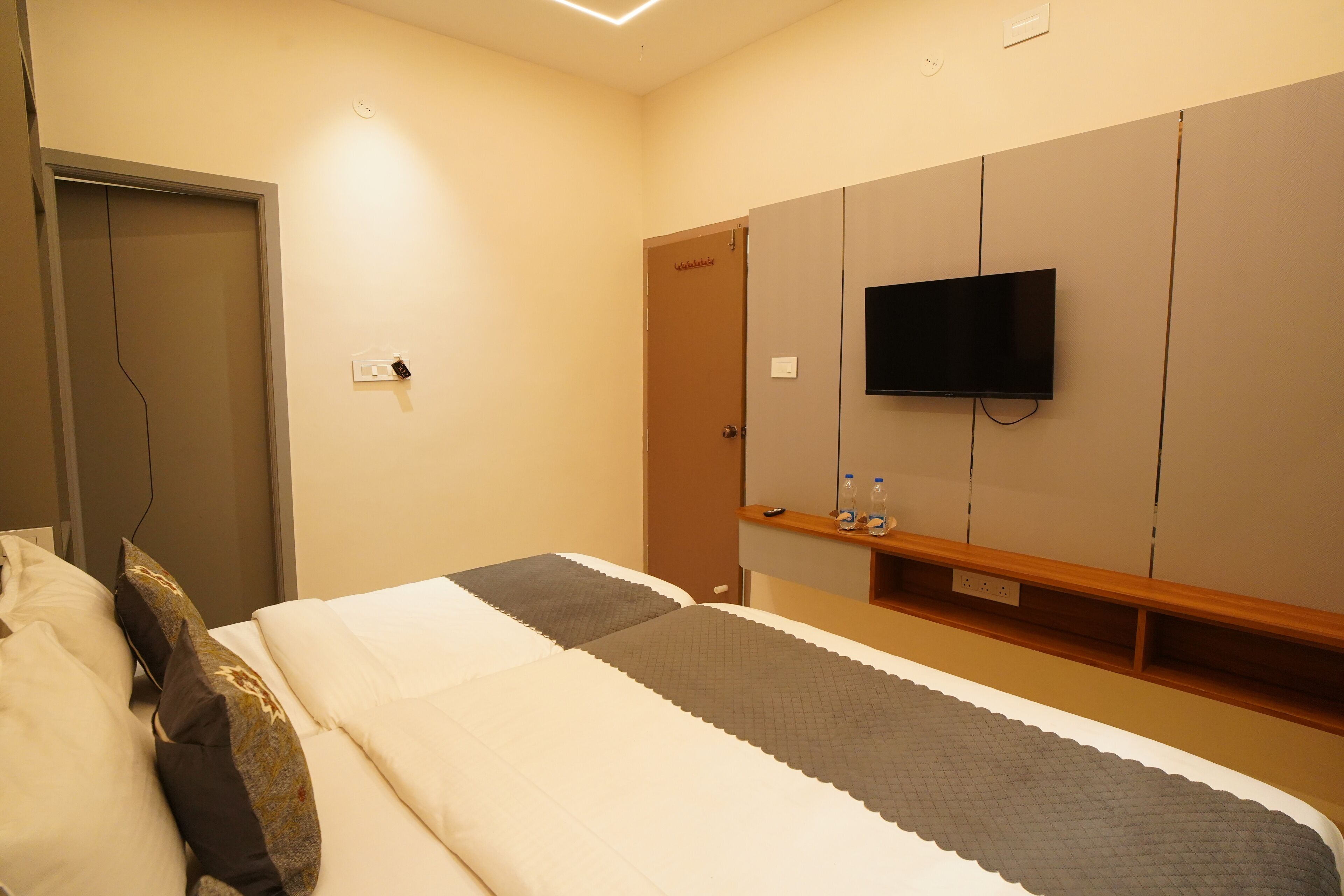 Une chambre d’hôtel avec un lit, un téléviseur fixé au mur et une porte.