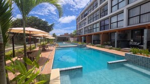 Un hotel moderno con piscina, mobiliario exterior y un patio cubierto.