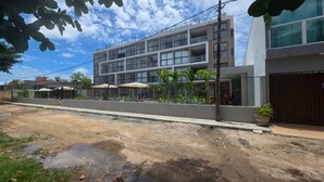 Un edificio moderno con varios pisos, ventanas amplias y un área de balcón con sombrillas.