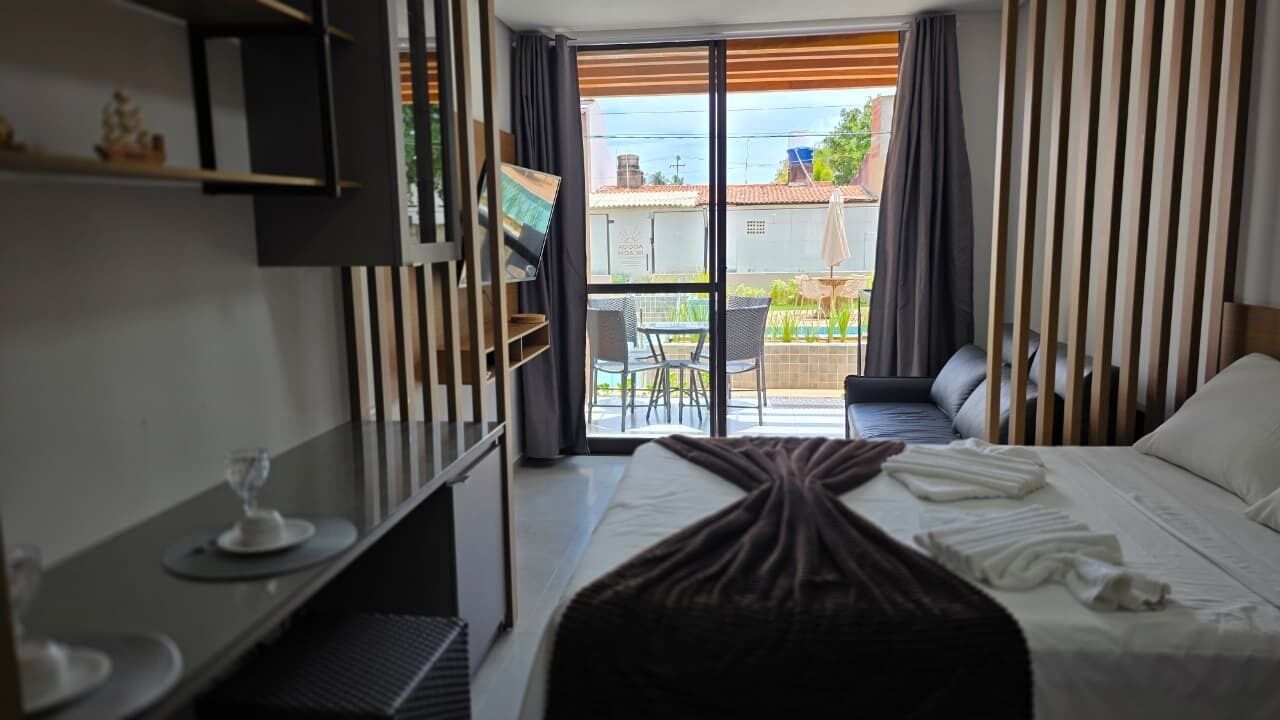 Una habitación de hotel con cama, escritorio y silla, televisor y balcón con mesa y sillas.
