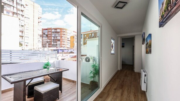 A balcony with a wicker table and bench, a sliding glass door, and a view of surrounding buildings.