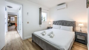 A bedroom with a large bed, a nightstand, an air conditioning unit, and a window with curtains.