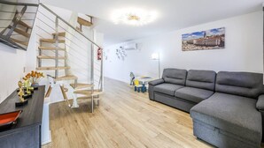 A modern living room with a grey sofa, a wooden staircase, and a cityscape painting on the wall.