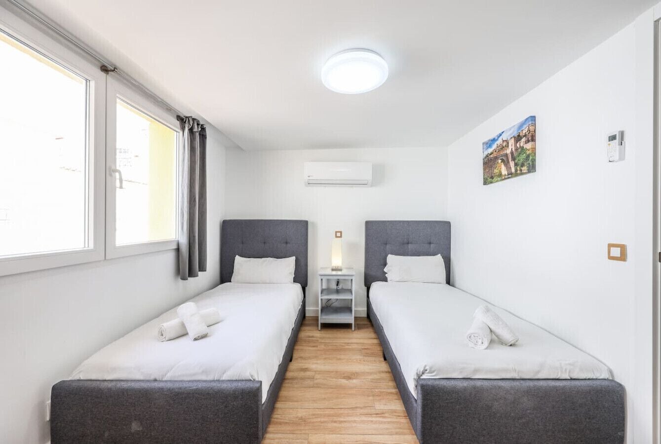 Een hotelkamer met twee enkele bedden, een klein nachtkastje, een airconditioning en een schilderij aan de muur.