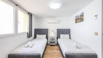 Een hotelkamer met twee enkele bedden, een klein nachtkastje, een airconditioning en een schilderij aan de muur.
