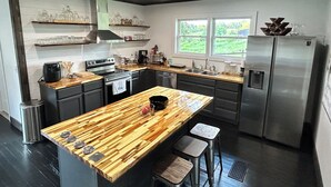 Een moderne keuken met een houten kookeiland, roestvrijstalen apparatuur en een raam dat voor natuurlijk licht zorgt.