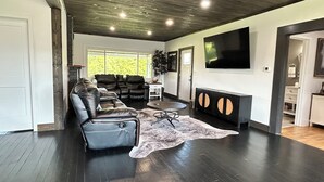 Een ruime woonkamer met een donker houten vloer, leren banken, een ronde salontafel en een grote flatscreen televisie aan de muur.