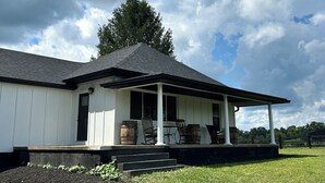 Een wit gebouw met een veranda en een trap, met een grote boom op de achtergrond.