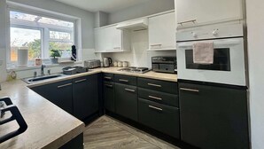 A modern kitchen with dark cabinets, a countertop, a sink, a stove, and an oven. - NEC Solihull Home | Parking, Garden, JLR & Airport (Solihull)