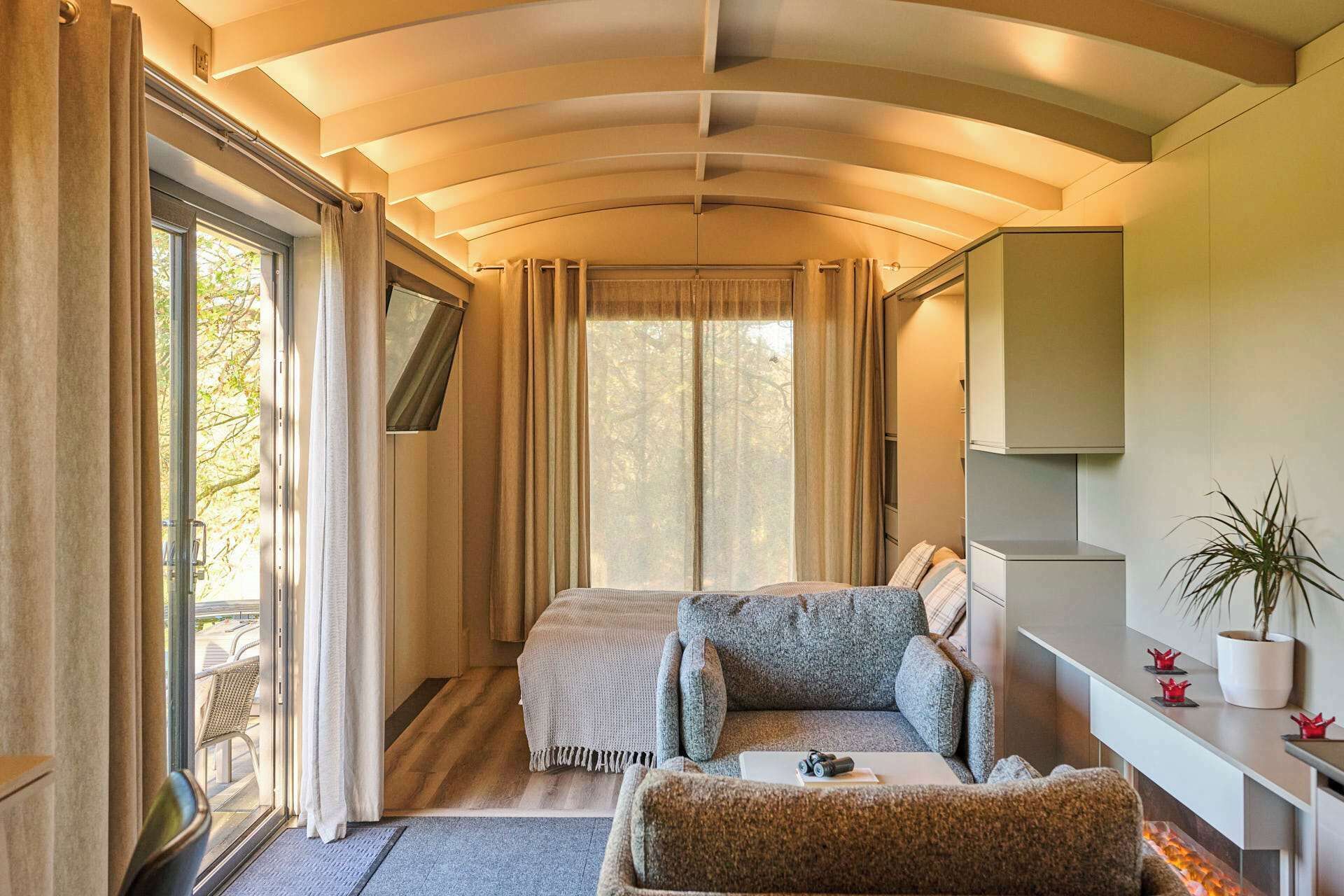 Une chambre confortable avec un lit, un canapé et un bureau. Il y a une fenêtre avec des rideaux, une plante et une petite table ornée d’objets décoratifs.