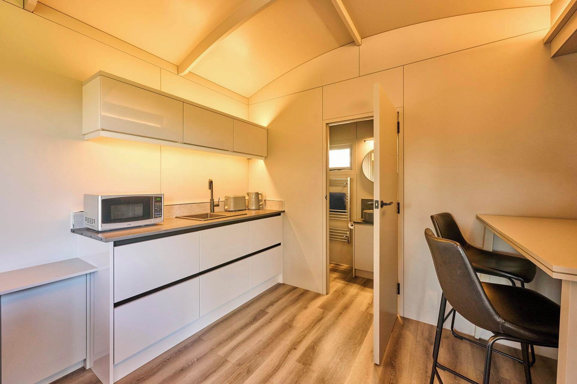 A compact kitchen with a microwave, sink, and bar stools.