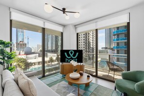 A modern living room with a sofa, a round coffee table, and a TV displaying the 'host' logo. Large windows offer a city view. - Condo City Crosby (Miami)