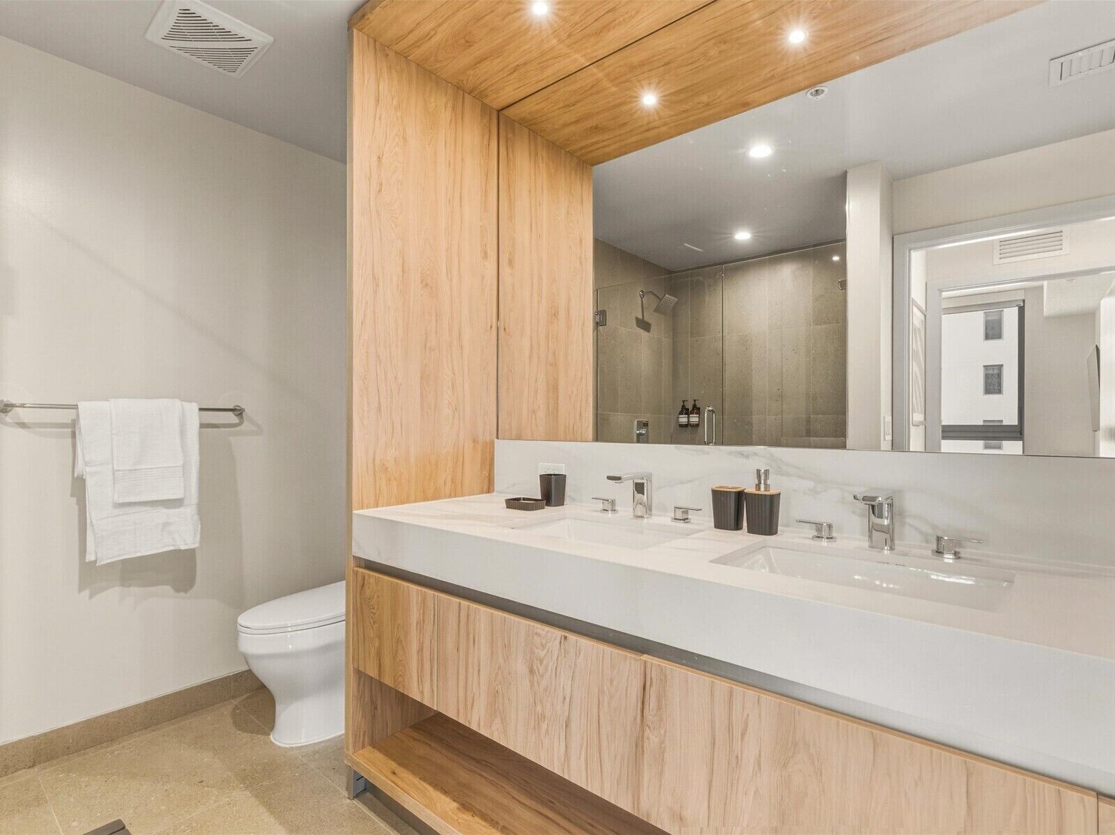 A modern bathroom with a wooden vanity, a large mirror, and a shower area.