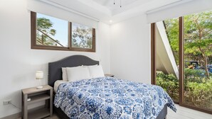 Ein Schlafzimmer mit Bett, Nachttisch und einem Fenster mit Blick auf Grünflächen.
