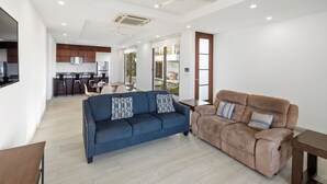 Ein modernes Wohnzimmer mit einer Couch, einem Couchtisch und einem Essbereich mit Stühlen, im Hintergrund eine Küche.