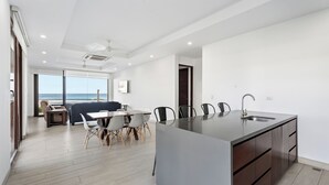 Eine moderne Küche mit einer zentralen Kochinsel, einem Essbereich mit Stühlen und Blick aufs Meer.