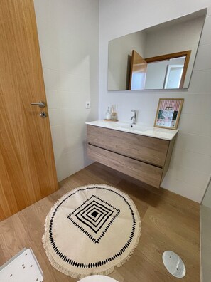 Un baño con una puerta de madera, un lavamanos blanco, un espejo y una alfombra decorativa.