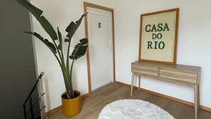 A hallway with a wooden floor, a potted plant, a white fluffy rug, a wooden bench, and a framed sign that reads "CASA DO RIO". - Charming Aguçadoura House, 2 Min to Beach • Garden & Pet-Friendly (Aguçadoura)