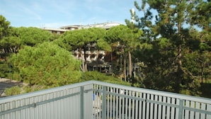 A building with a white facade and multiple windows, surrounded by dense green trees. - Apartment 50mt From the Beach (Lignano Sabbiadoro)