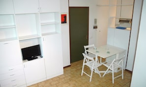 A compact kitchen with white cabinets, a small dining table with chairs, and a television. - Apartment 50mt From the Beach (Lignano Sabbiadoro)
