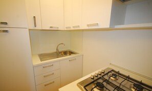 A kitchen with white cabinets, a stainless steel sink, and a gas stove. - Apartment 50mt From the Beach (Lignano Sabbiadoro)