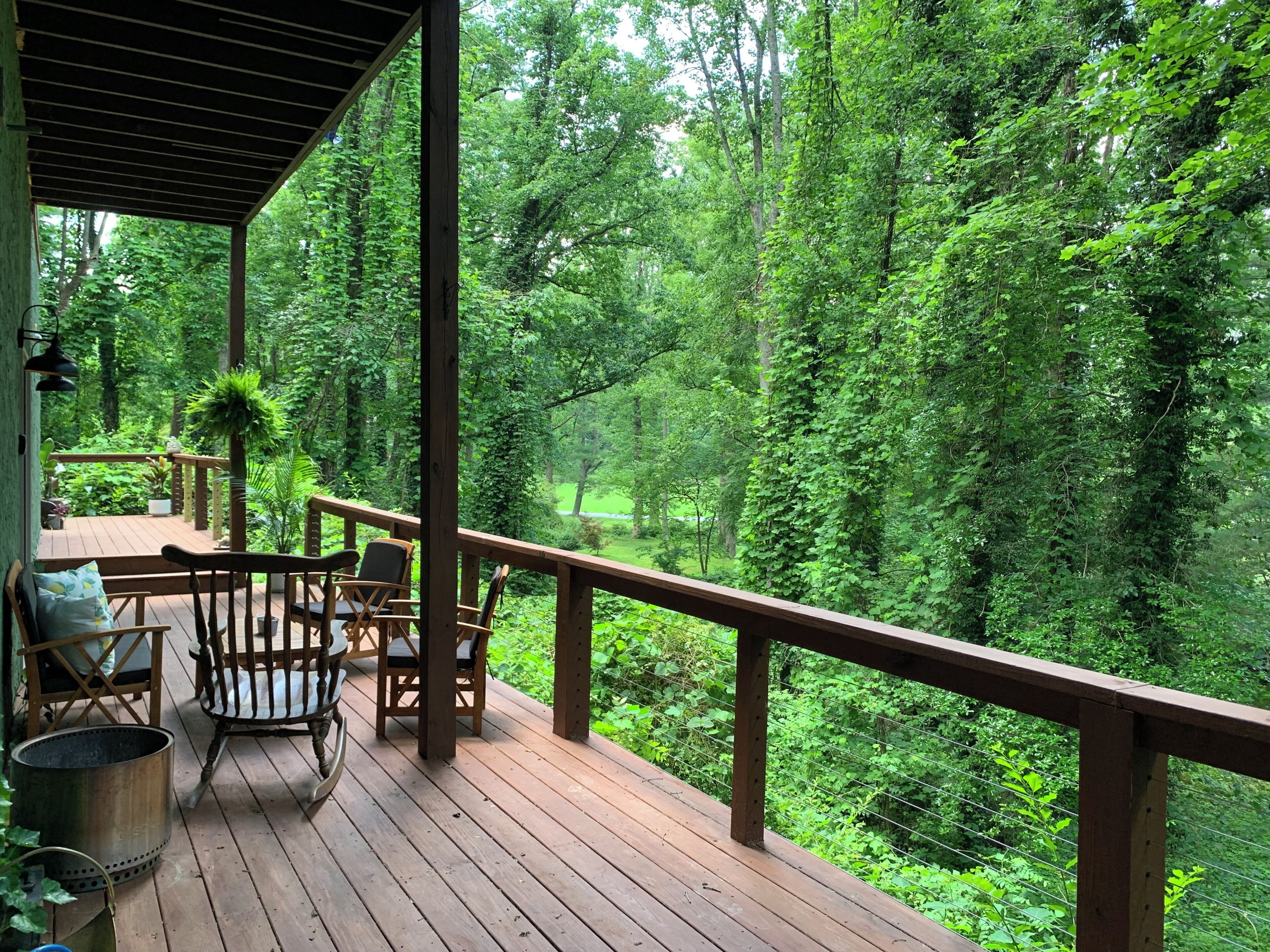 A wooden deck with chairs and a table, overlooking a dense forest.