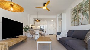 A modern living room with a flat-screen TV, a wooden coffee table, a grey sofa, a ceiling fan, and a dining area with wicker chairs. - Casa Marta - Seaviews (Torremolinos)