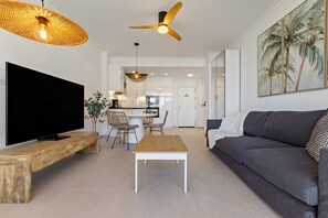 A modern living room with a flat-screen TV, a wooden coffee table, a grey sofa, a ceiling fan, and a dining area with wicker chairs. - Casa Marta - Seaviews (Torremolinos)