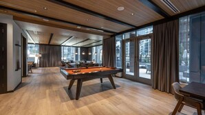 Une pièce spacieuse équipée d’une table de billard, de sièges confortables et de grandes fenêtres donnant sur l’extérieur.