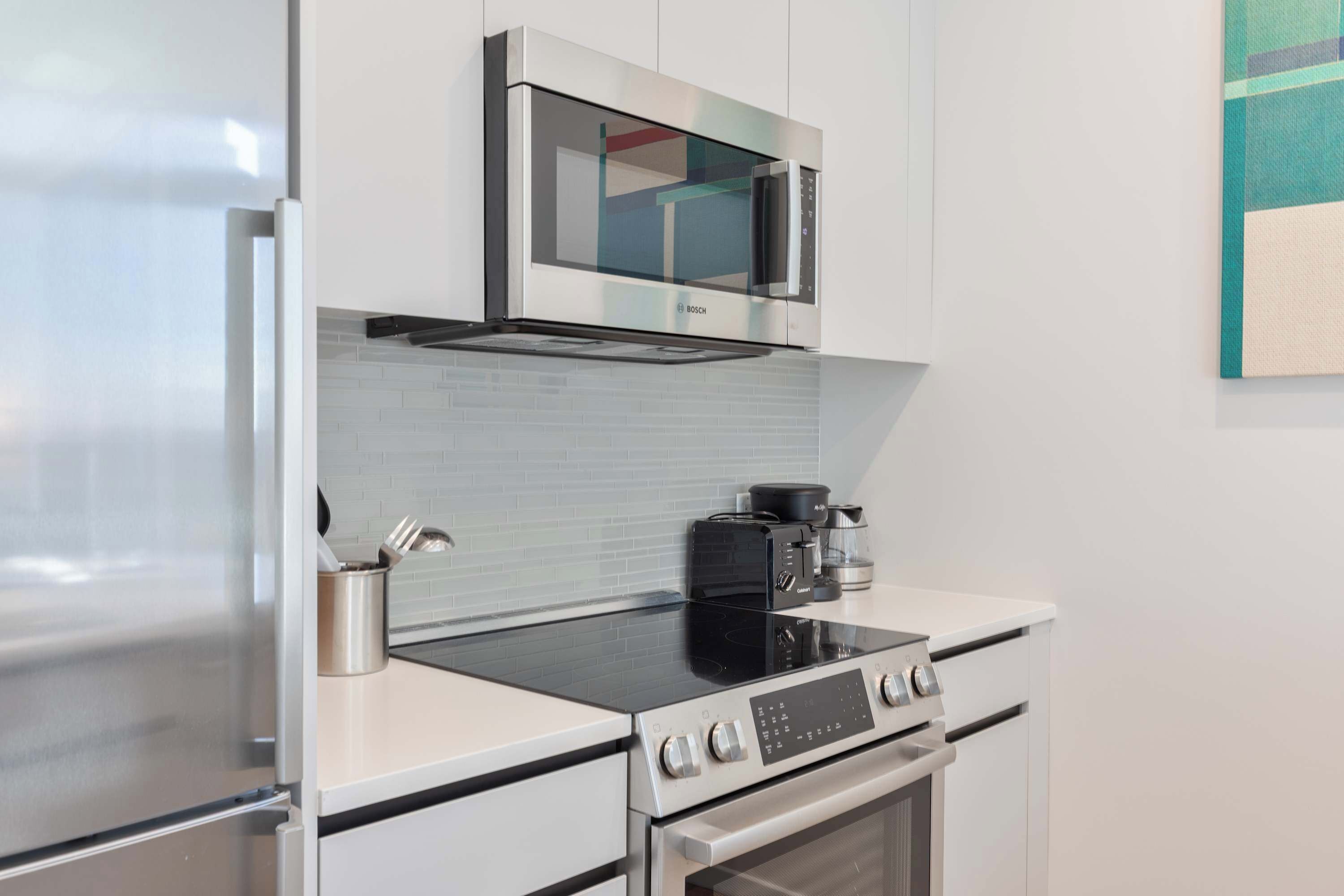 A modern kitchen with a stainless steel refrigerator, Bosch microwave, and a black induction cooktop.