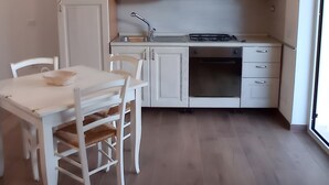 A compact kitchen with white cabinetry, a dining table with chairs, and a large window. - Apartment 'Casa Del Mirto' with Private Terrace, Wi-Fi and Air Conditioning (Olbia)