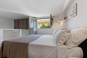 A single bed with a white mattress and pillows, a brown throw blanket, a window with curtains, and a wall-mounted light fixture. - Apartment 'Casa Del Mirto' with Private Terrace, Wi-Fi and Air Conditioning (Olbia)