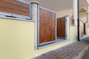 Une rangée de portes en bois fermées, dotées de montures métalliques, se dressent sur un mur jaune, avec un chemin pavé en briques.