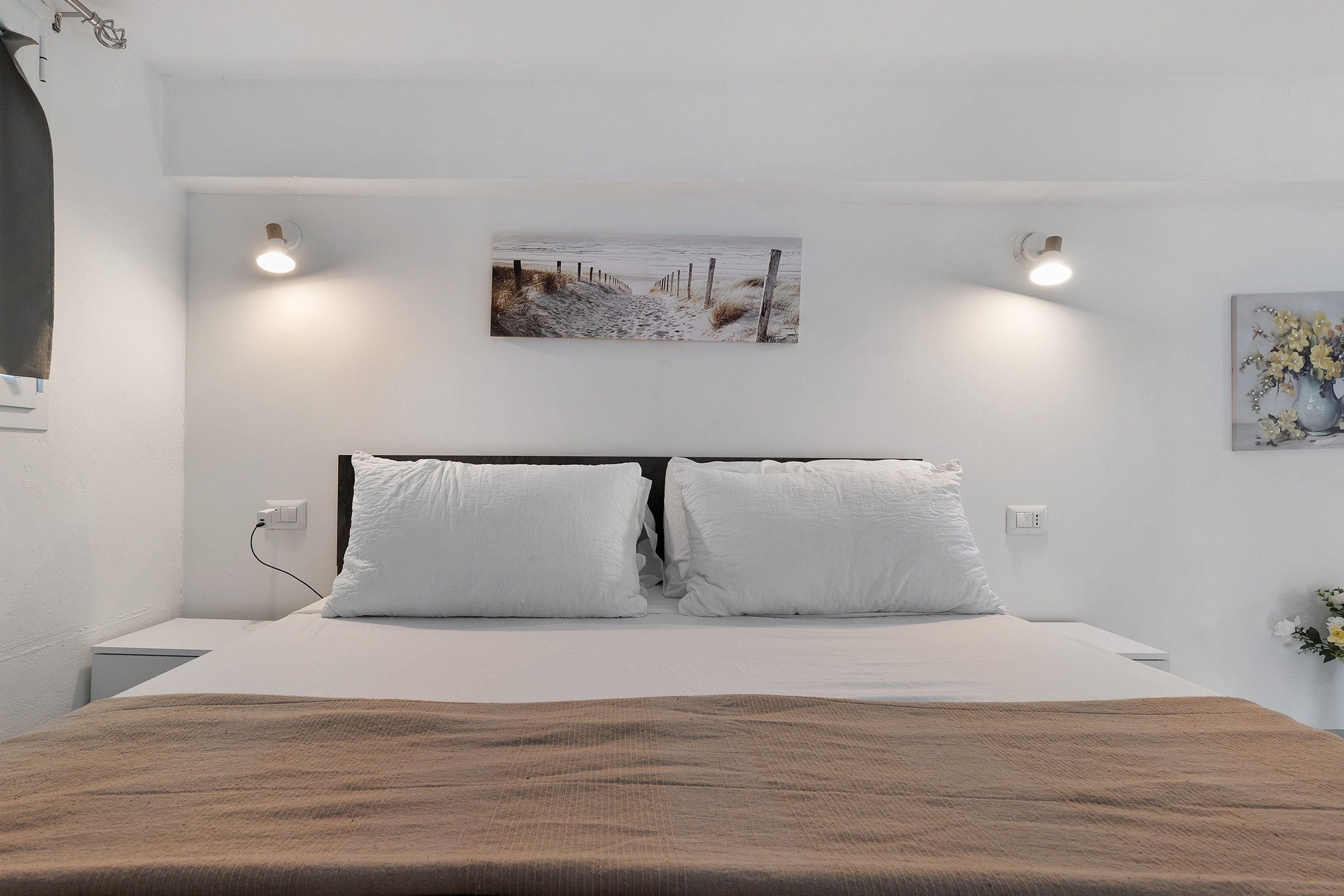 Ein Schlafzimmer mit einem Bett, zwei Nachttischlampen, einem Gemälde an der Wand und einer Steckdose.