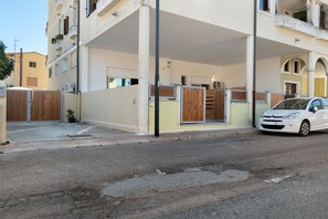 A residential building with a covered parking area, a white car parked in front, and a visible apartment entrance. - Apartment 'Casa Del Mirto' with Private Terrace, Wi-Fi and Air Conditioning (Olbia)