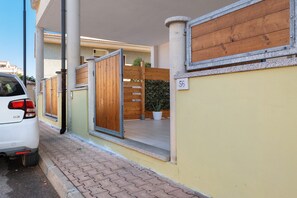 A gated entrance with a wooden door, a potted plant, and a building number sign. - Apartment 'Casa Del Mirto' with Private Terrace, Wi-Fi and Air Conditioning (Olbia)