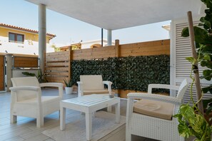 An outdoor patio area with wicker furniture, a wooden fence, and a wall covered with foliage. - Apartment 'Casa Dell'Oleandro' with Private Terrace, Wi-Fi and Air Conditioning (Olbia)