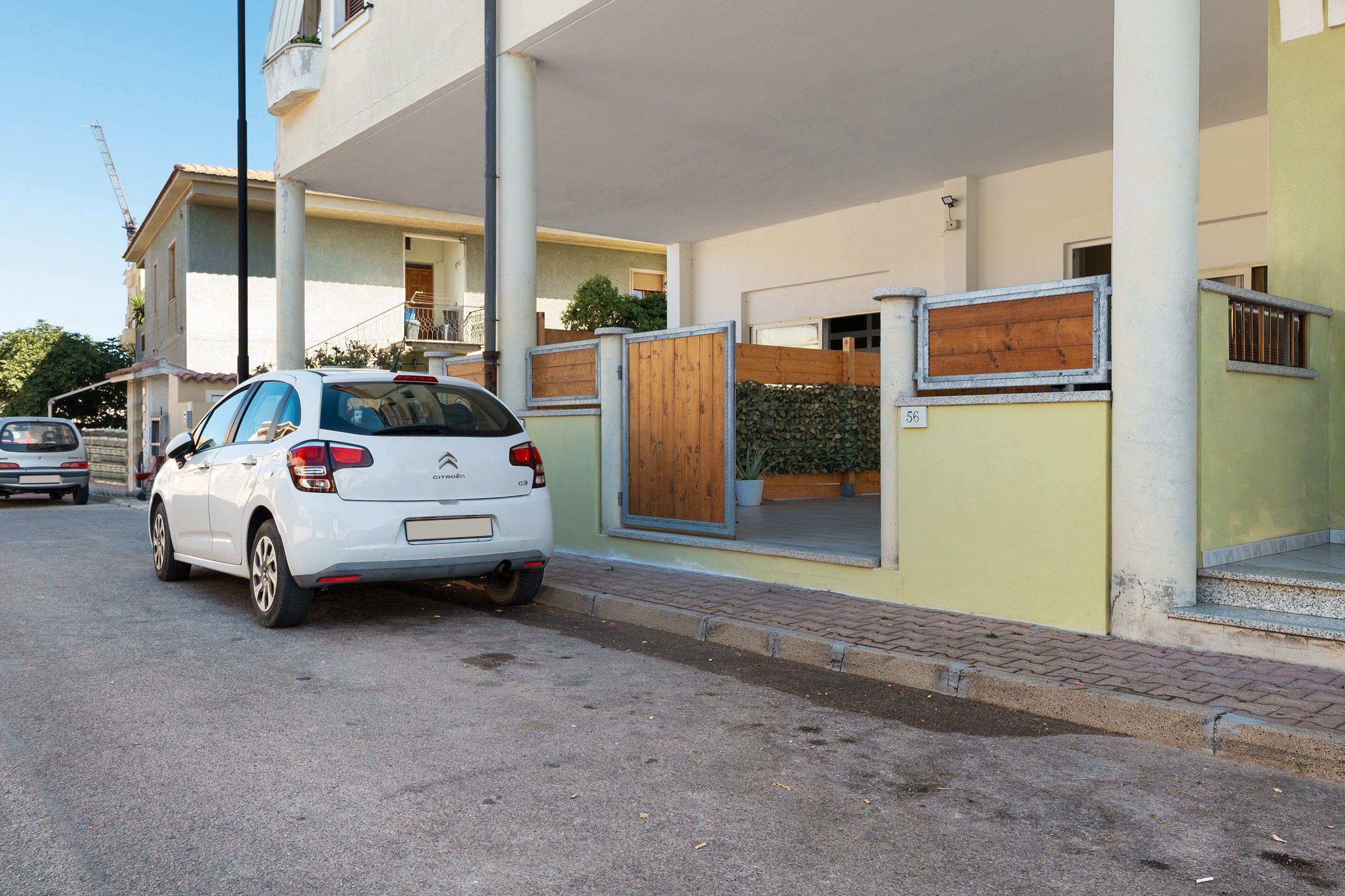 A white Citroen car parked in front of a building with a gated entrance, a visible number '56', and a paved driveway.