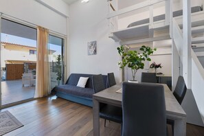 Ein modernes Interieur mit einer Couch, einem Esstisch, Stühlen, einer Treppe und einer Schiebeglastür zu einem Außenbereich.