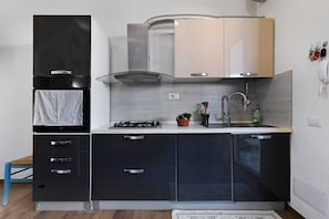 A compact kitchen with a gas stove, a sink, and a range hood. There are cabinets with handles and a small potted plant on the counter. - Apartment 'Casa Dell'Oleandro' with Private Terrace, Wi-Fi and Air Conditioning (Olbia)