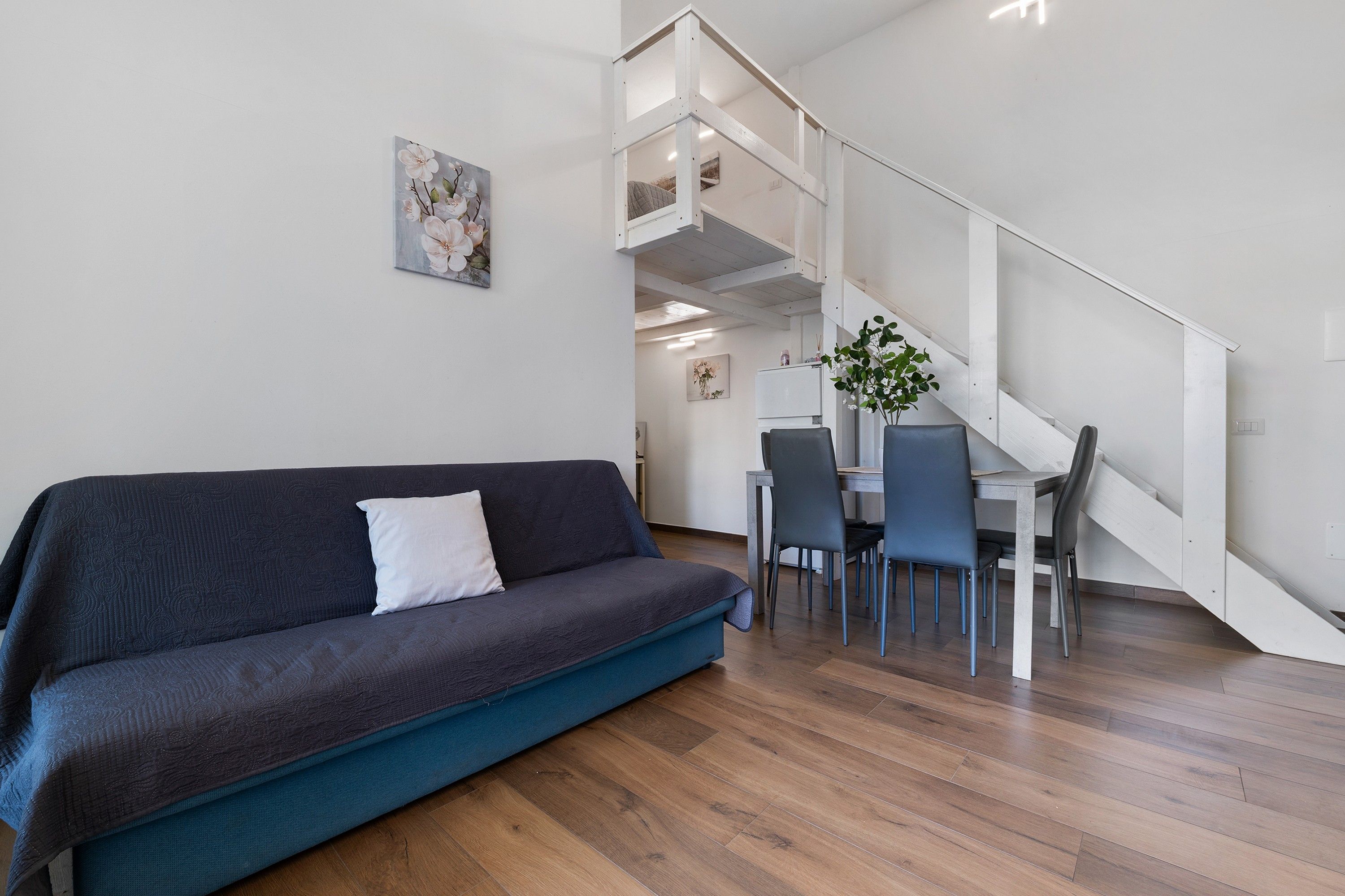 Een moderne woonkamer met een donkerblauwe bank, een wit kussen en een houten vloer.